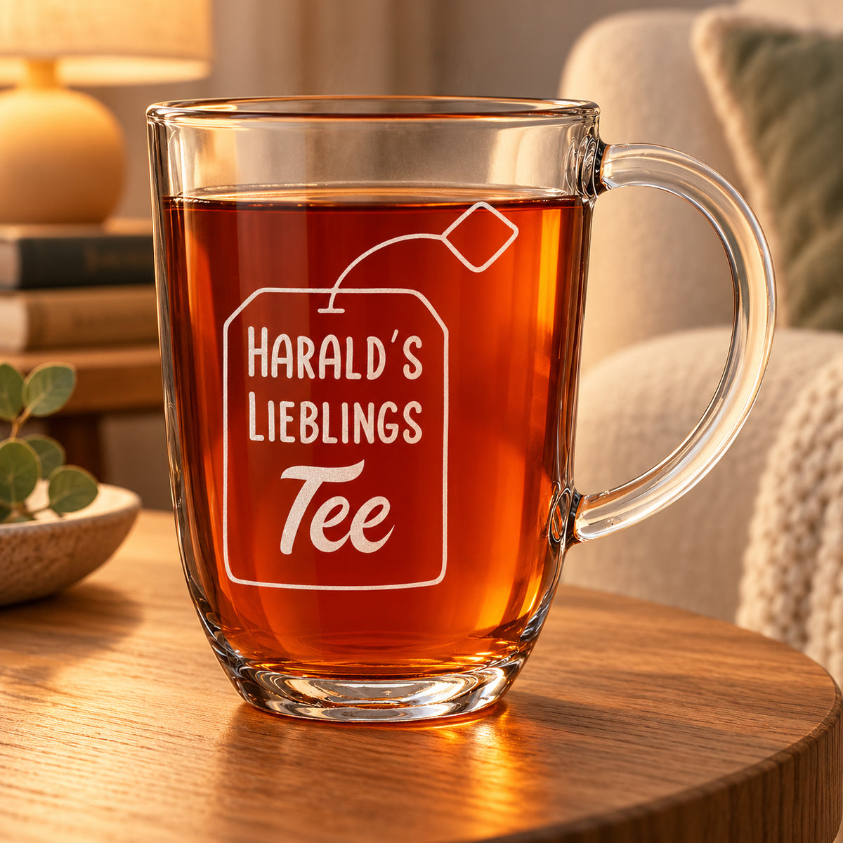 Teeglas mit Lieblingstee-Gravur und Beispielname Harald auf einem Beistelltisch neben einem Sessel