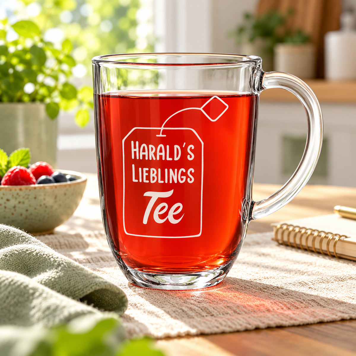 Personalisiertes Teeglas mit rotem Früchtetee auf einem hellen Tisch am Küchenfenster
