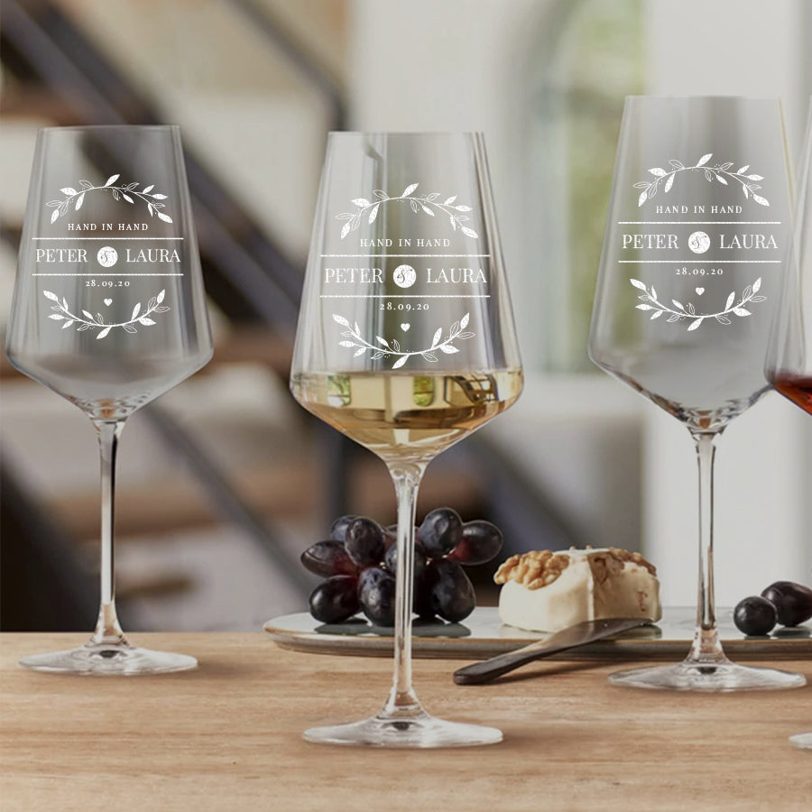 Zwei elegant gravierte Weißweingläser auf einem weißen Tisch neben kleinen Gourmet-Vorspeisen Löffeln mit Pasta.