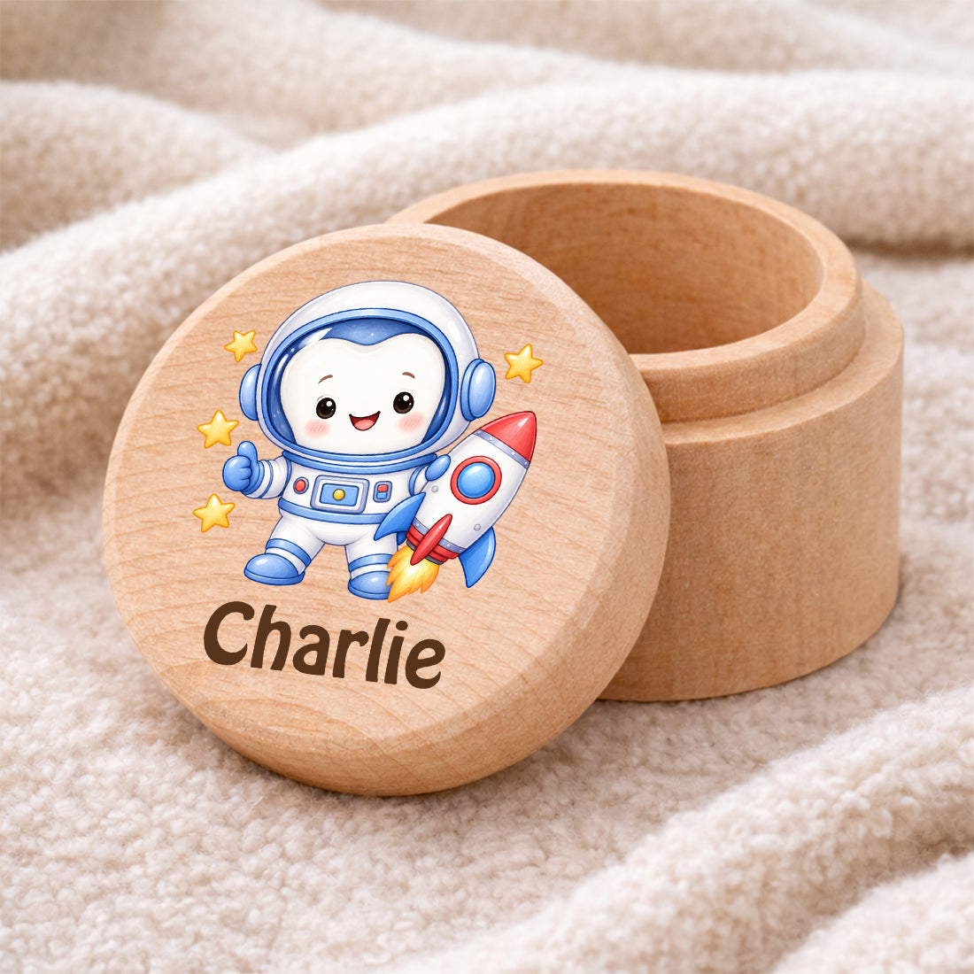 Runde Zahndose mit Motiv Zahn-Astronaut und Beispielname Charlie auf einer weichen Decke