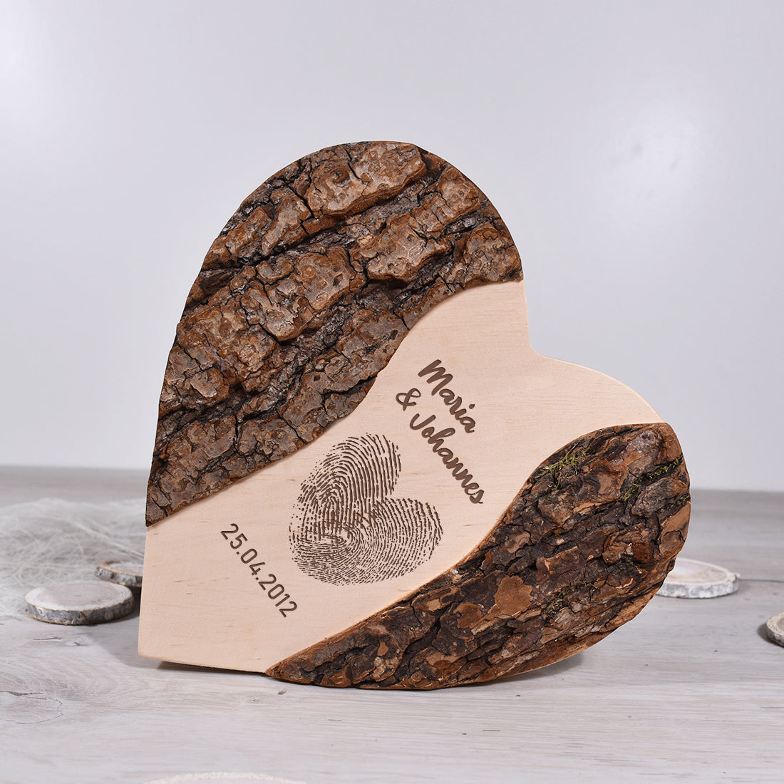 Nahaufnahme der gravierten Holzoberfläche mit Namen, Datum '25.04.2012' und Fingerabdruck-Herz, umrahmt von natürlicher Baumrinde.