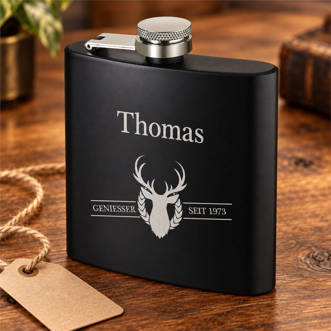 Schwarzer Genießer-Flachmann mit Beispielname Thomas und Jahreszahl 1973 in einer Geschenkszene.