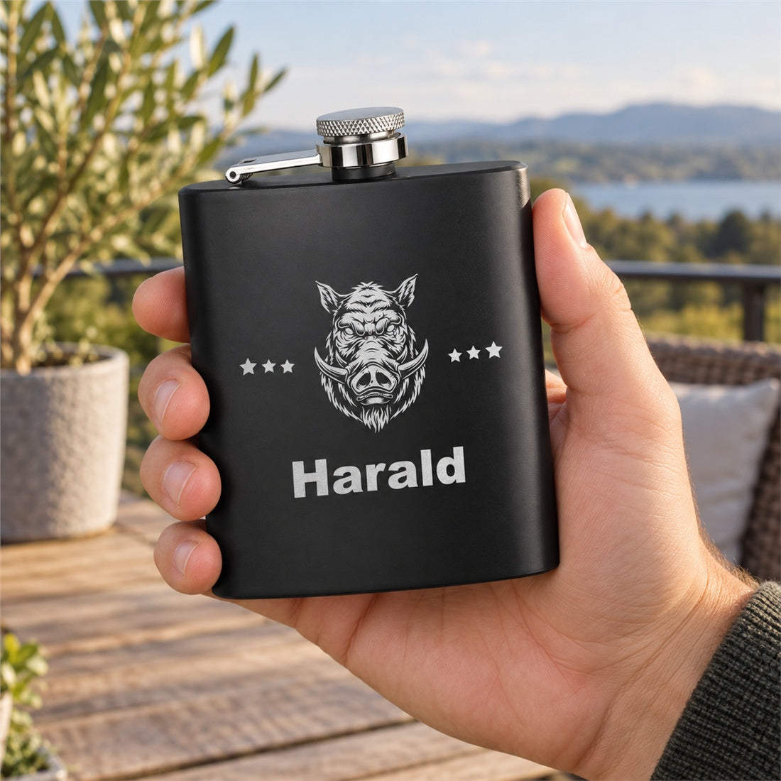 Eine Hand hält den schwarzen Flachmann mit Wildschwein-Motiv und Beispielname Harald.