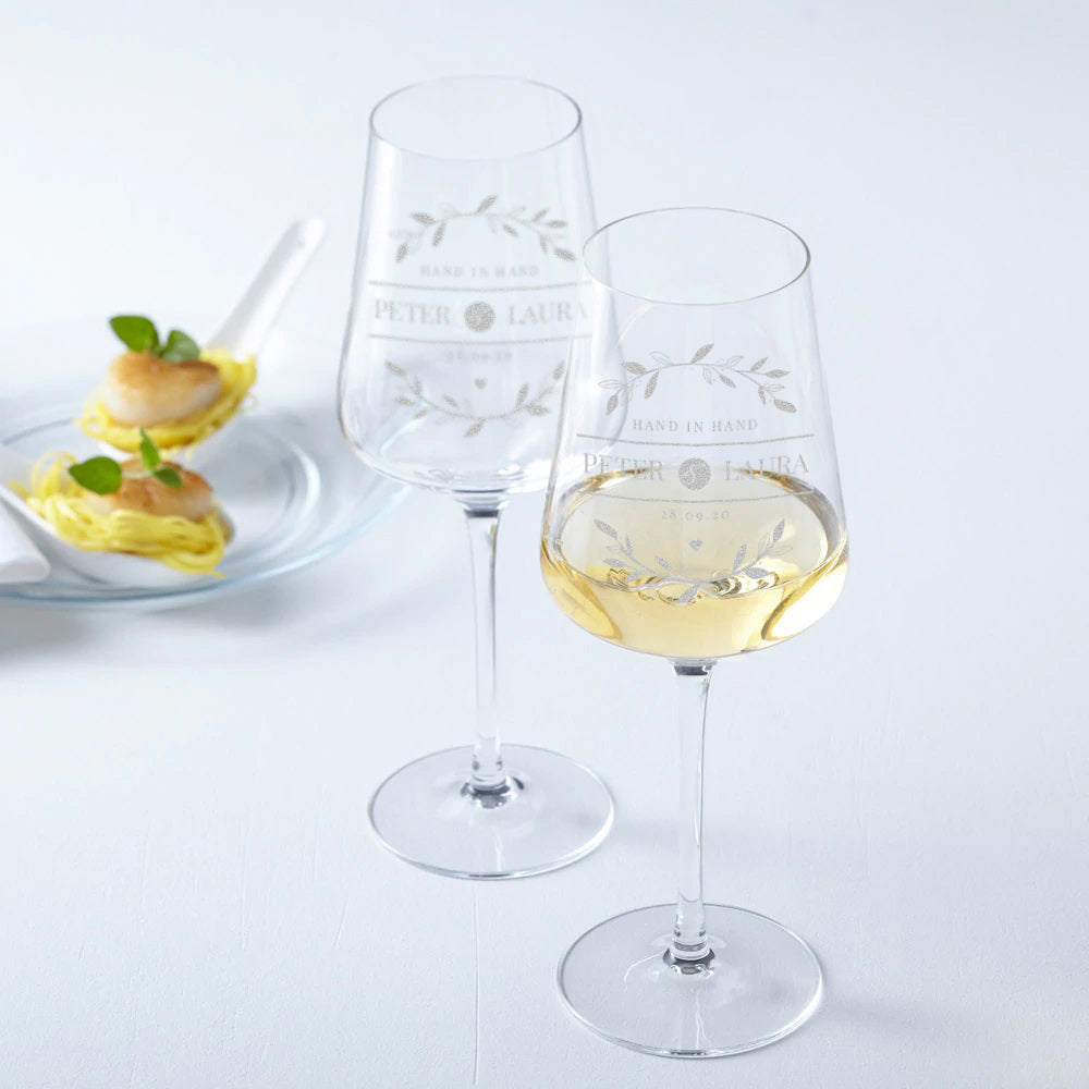 Ein Set aus zwei personalisierten Weingläsern mit feiner Lasergravur und einer frischen Traube grüner Weintrauben auf weißem Hintergrund.