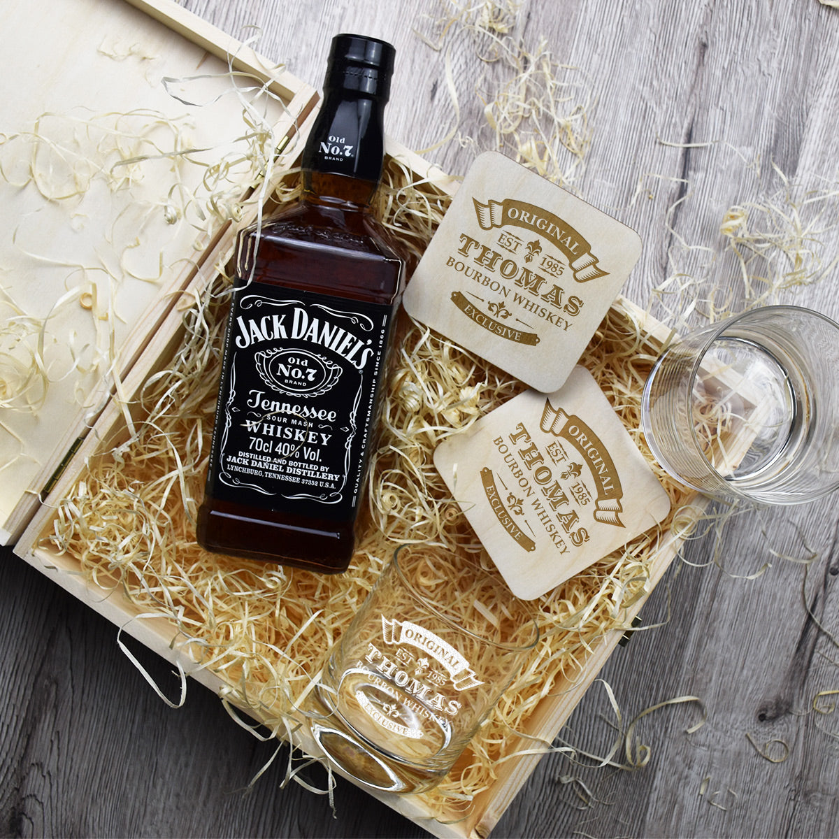 Geöffnete personalisierte Holzbox mit Holzwolle, zwei Jack Daniels Flaschen und gravierten Gläsern in der Draufsicht.